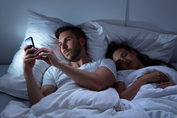 07 young man using cellphone while her wife is sleeping