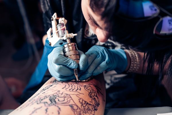 tattoo artist demonstrates process getting tattoo on leg