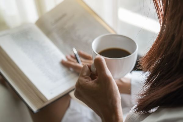 woman holding coffee reading book beside window