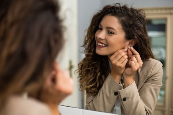happy woman putting earrings in front mirror