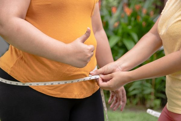 woman thumbs up friend using tape measure waist
