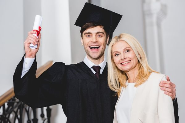cheerful son graduation cap holding diploma with mother