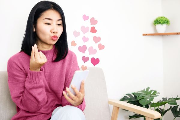 asian woman using mobile phone posing giving heart sign