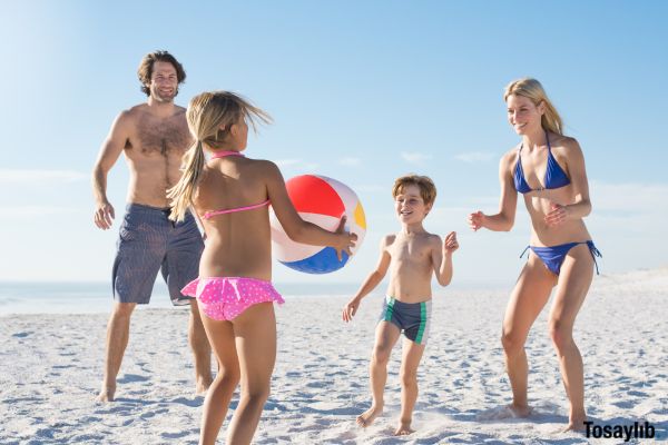 family playing beach ball toss game on beach
