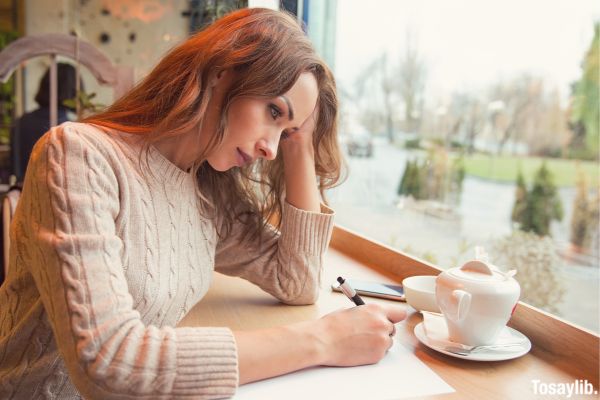 Young female writer writing sad articles in cafe