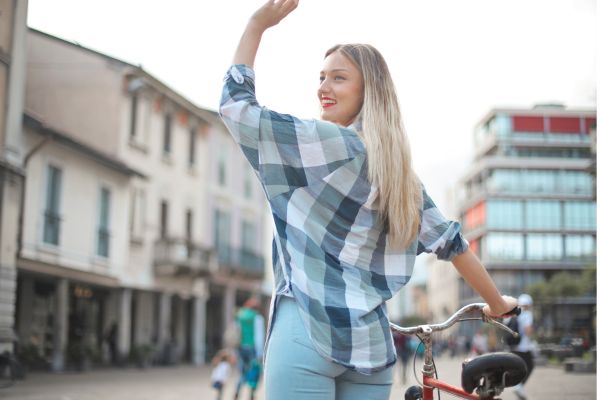 Smiling Woman in Jeans Standing with a Bicycle Waving Goodbye